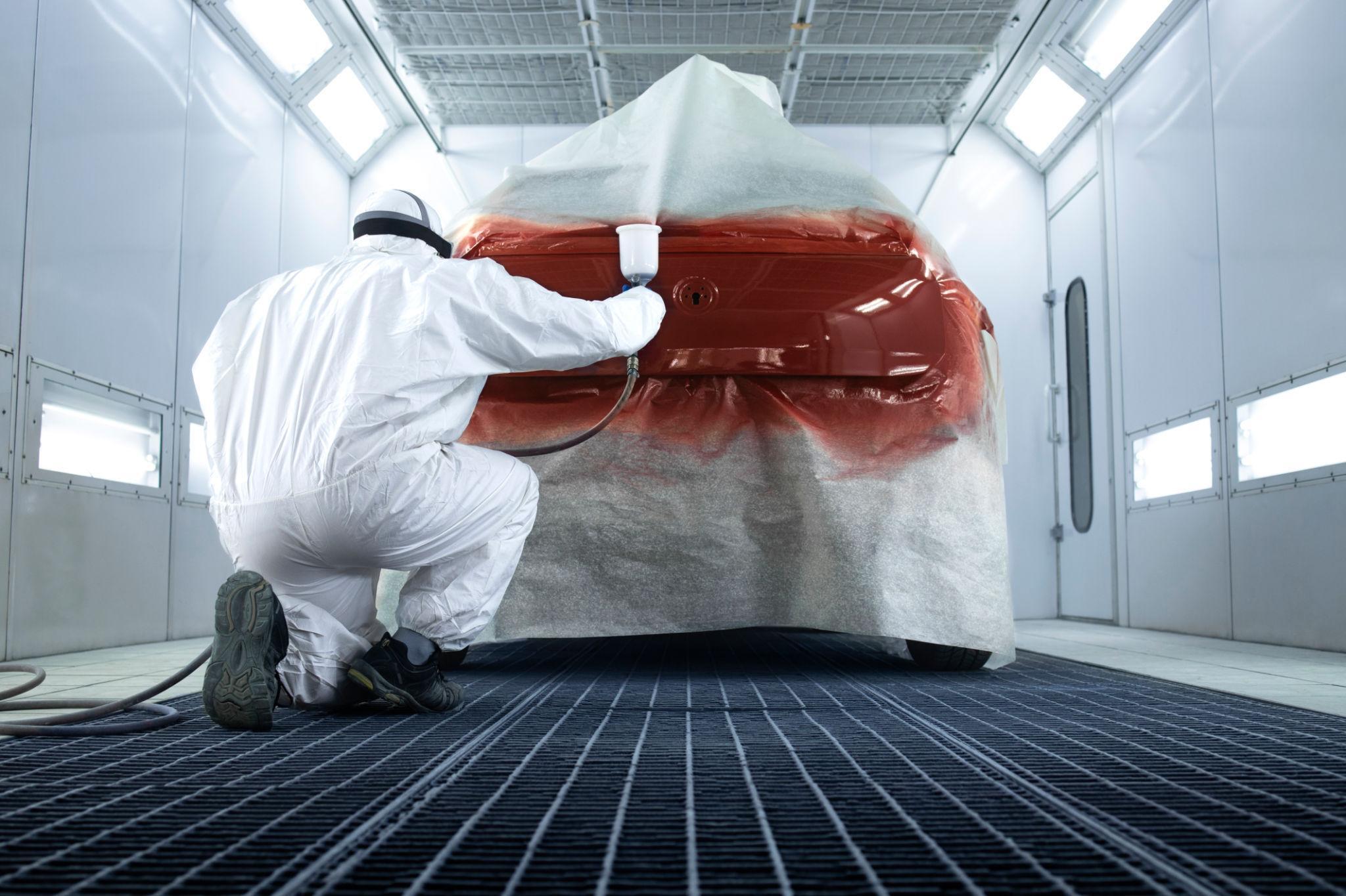 Técnico pintando coche en cabina profesional